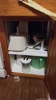 Cabinet upper shelf showing white food processor with bowl and discs alongside accessories