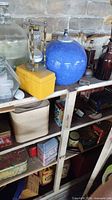 Shelf with blue ceramic globe, hourglass, yellow box, clear jug, amber bottles and assortment of tins