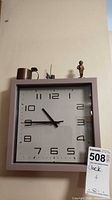 Square wall clock with metal cup, figurine and small objects on top