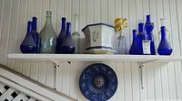 Shelf with multiple cobalt blue and clear bottles, planter, bud vase, wall plaque