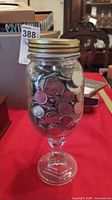 Full view of glass jar filled with coins mounted on goblet stem