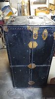 Front view of black Madison steamer trunk showing brass hardware and riveted panels