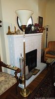 Full view of brass floor lamp with glass shade beside fireplace