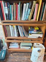 Full bookcase showing three shelves packed with books, magazines and spiral notebooks plus shopping bag