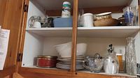 Cabinet shelves showing variety of glassware, plates, bowls, jars