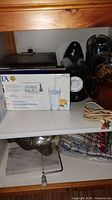Shelf showing boxed Brita pitcher, waffle iron, other items
