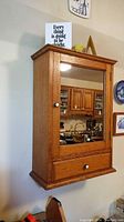 Front view of oak medicine cabinet mounted on wall showing mirrored door and lower drawer