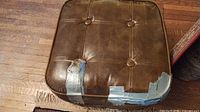 Top view of brown leather ottoman showing tuft buttons and duct tape repairs