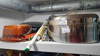 Stainless steel roasting pan, ceramic dish, grill lid, fluorescent tubes grouped on shelf