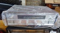 Front view of Rotel FAX-220W receiver wrapped in plastic showing silver faceplate and knobs