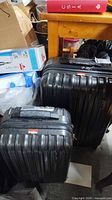 Two black hard-shell suitcases side by side under a wooden table