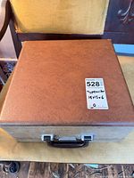 Closed brown hard case with label showing lot number and dimensions