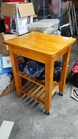 Front/side view of wooden kitchen cart showing butcher block top, slatted shelf, casters