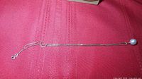 Full view of sterling silver box-chain necklace with pearl pendant and spring ring clasp on fabric background