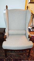 Front view of beige wingback chair showing upholstery, wood frame, lumbar pillow