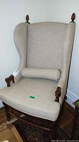 Front view of beige wingback chair showing upholstery, wood frame and lumbar pillow