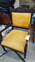 Front view of armchair showing carved crest, yellow velvet upholstery, casters