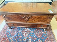 front view of blanket chest showing carved appliqué, lower drawer, bun feet