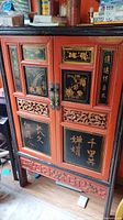 Front view showing red lacquer doors, black gilt panels, brass handles, carved friezes