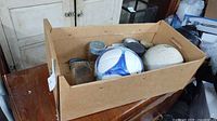 Cardboard box on dresser containing jars, balls and lids