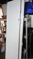Full view of white louvered door leaning against shelf, hinges visible