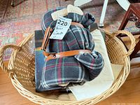 Basket containing rolled dark plaid blanket strapped with leather and book