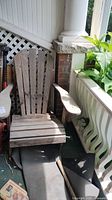 Angled view of weathered wooden Adirondack chair on porch