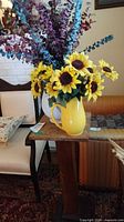 Wood pedestal stand with yellow pitcher of flowers beside chair