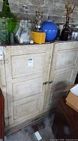 Front view of cabinet with doors closed showing distressed paint and hardware