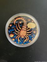 Obverse showing enameled Scorpio design inside plastic capsule
