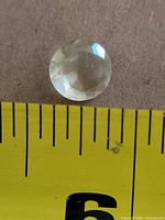 Top view of round faceted transparent gemstone beside tape measure for scale