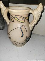 Full view of cream ceramic urn with bird handles and painted motifs