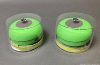 Two sealed green waterproof Bluetooth speakers in clear cylindrical cases