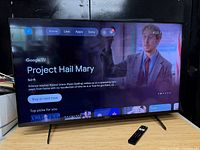 Front view of Sony XR-50X90J TV powered on displaying Google TV interface with remote positioned in front