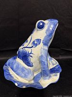 Front three-quarter view of blue and white porcelain frog figurine showing floral decoration and lily-pad base
