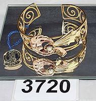 Two-tone gold filled floral cuff bracelet with attached Harry Isken tag displayed on reflective surface