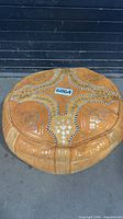 Top view of round tan/orange leather pouf with gold patterns