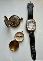 Group view: Diesel wristwatch, hunter pocket watch open, open compass with lid, compass lid
