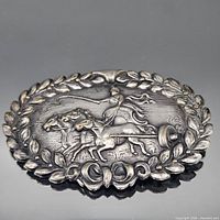 Front view of oval silver-tone pin with chariot and laurel motif