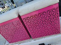 Two pink metal cube ottomans with white cushions, showing decorative cut-out sides