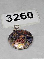 Front view of round purple cloisonné enamel pendant showing floral and butterfly design with gold-tone bail
