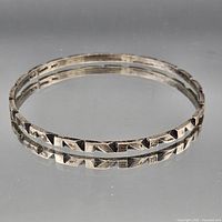 Two sterling silver bangles with geometric oxidized design displayed side by side