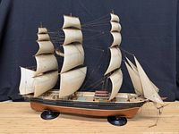 Full view of ship model on twin black stands showing sails, hull and rigging