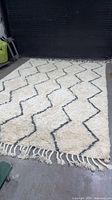 Full view of large ivory shag rug with charcoal zigzag pattern and fringe