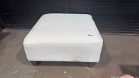 Front view of square ivory ottoman on wood legs