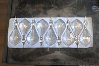 Tray holding eight clear faceted chandelier crystals with attached octagon gems and brass bowties