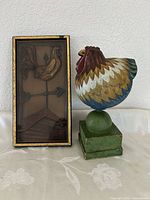 Wooden rooster sculpture beside framed metal weather vane rooster art
