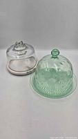 Clear glass cloche on marble base beside green glass cloche with plate