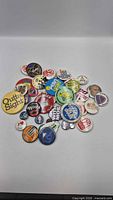 Pile of approximately 35 assorted round pin-back buttons on white background
