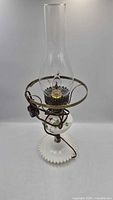 Full view of electric oil-style lamp showing milk glass base, floral design, brass-tone ring and clear chimney